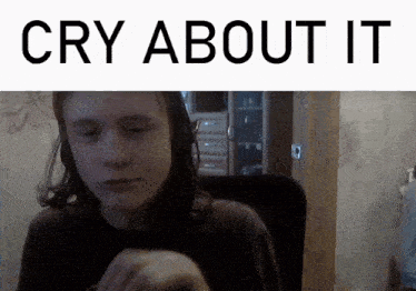 a young man is sitting in front of a screen that says " cry about it "