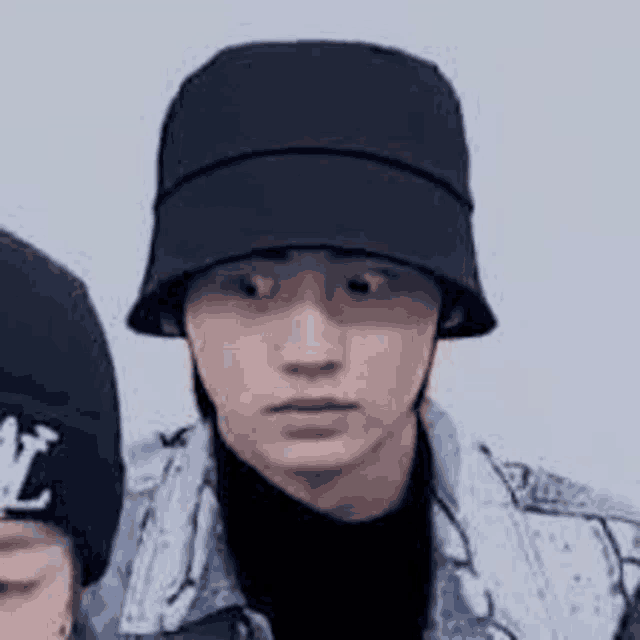 a man wearing a black hat and a denim jacket is standing next to another man .