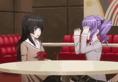 two anime girls are sitting at a table in a restaurant .