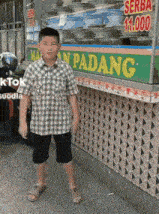 a young boy stands in front of a man padang food stand