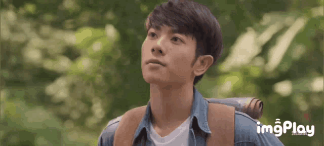 a young man with a backpack looks up at the sky with imgplay in the corner