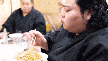 a man eating noodles with chopsticks while another man looks on