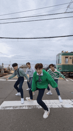 a group of young men are dancing on a street in front of a train that says tokyo