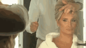 a woman is getting her hair done by a man in a white robe .