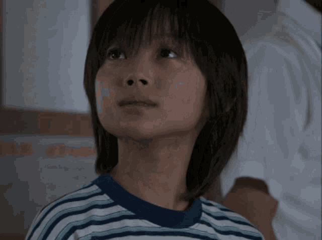 a young boy wearing a striped shirt looks up at something