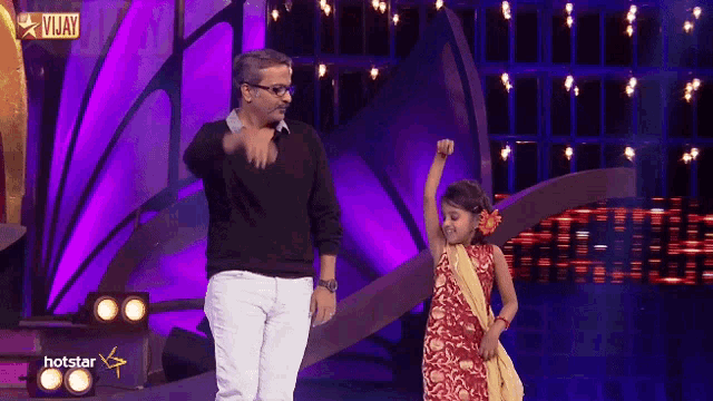 a man and a little girl are dancing on a stage with a hotstar logo in the background