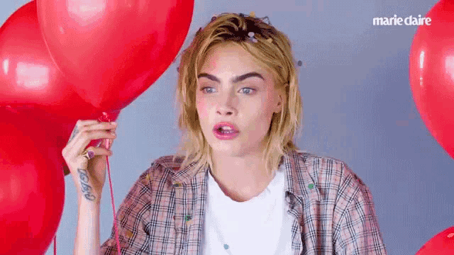a woman in a plaid shirt is holding a red heart shaped balloon in her hand .