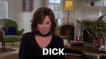 a woman is sitting in a living room with the word dick written on her chest .