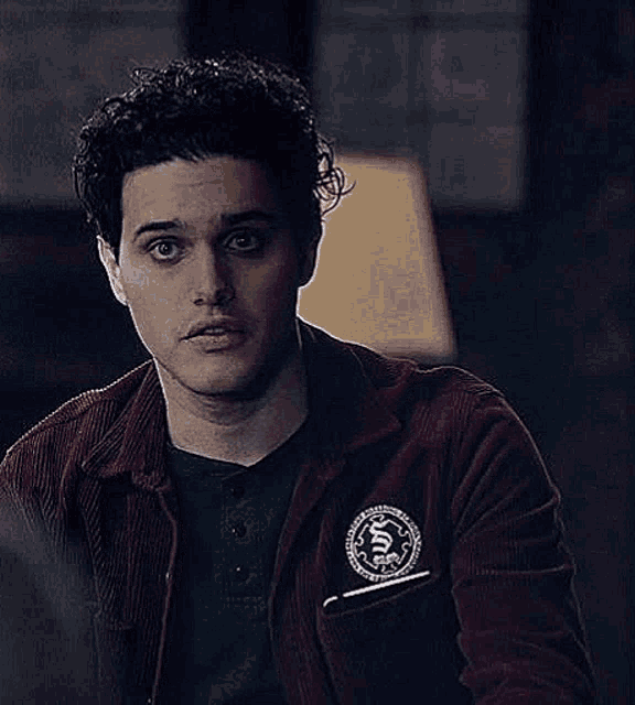 a young man with curly hair is wearing a red jacket and a black shirt .