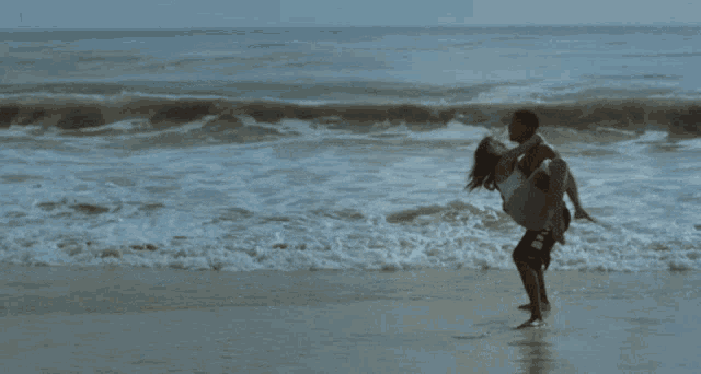 a man is carrying a woman in his arms on a beach