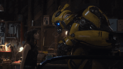 a woman stands next to a yellow robot in a dark room