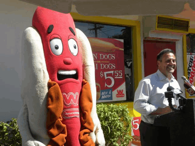 a man stands in front of a sign that says hot dogs