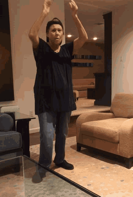 a woman in a black shirt is standing in a living room with her arms in the air