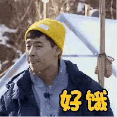 a man wearing a yellow beanie is standing in front of a tent ..