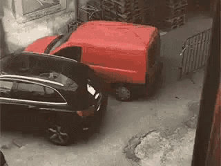 a red van and a black car are parked in a parking lot .