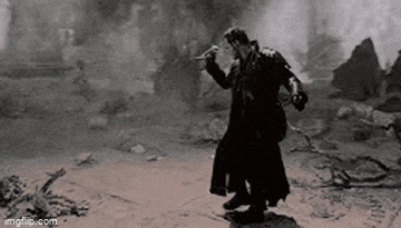 a black and white photo of a man in a trench coat standing on a dirt road .