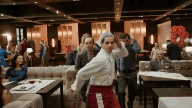 a man in a white shirt and red pants is dancing in a restaurant with other people