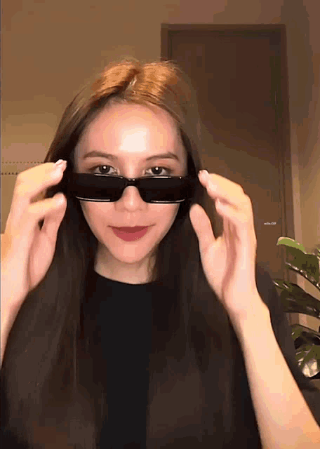 a woman wearing sunglasses is standing in front of a door that says ' a ' on it