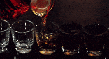 a row of shot glasses are lined up on a table with a bottle in the background