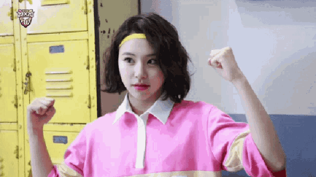 a girl in a pink shirt is flexing her muscles in front of yellow lockers