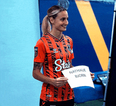 a woman in an orange and black striped shirt is holding a piece of paper with the name nathalie bjorn on it