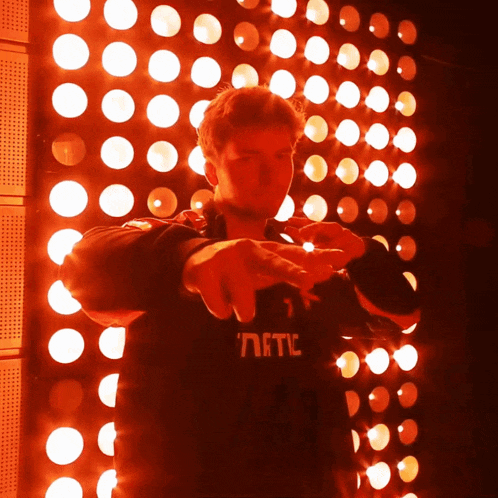 a man wearing a black shirt that says ' nftc ' on it stands in front of a wall of red lights