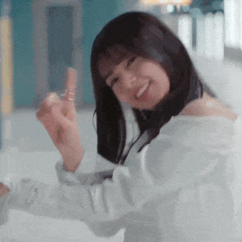 a woman in a white off the shoulder shirt is holding a bottle of lipstick and smiling .