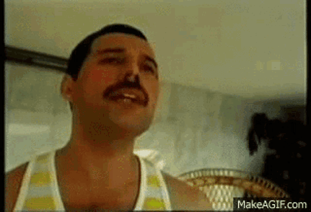 a man with a mustache is wearing a striped tank top and making a funny face .