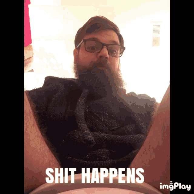 a man with glasses and a beard is sitting on a toilet with the words " shit happens " below him