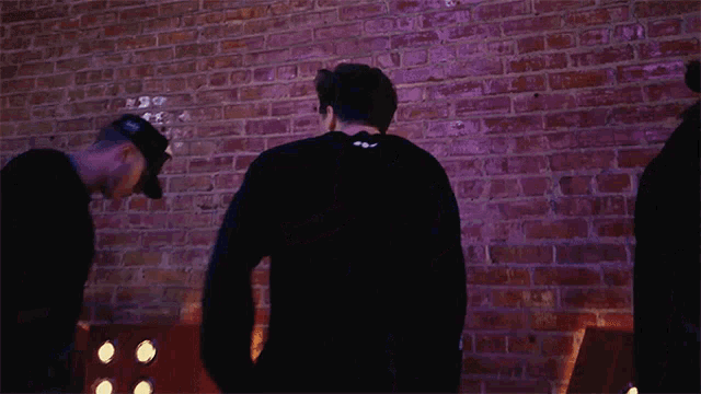 three men are dancing in front of a brick wall and a red letter a