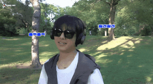 a young man wearing headphones and sunglasses stands in a park with trees and grass