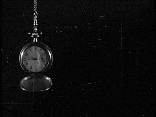 a black and white photo of a pocket watch hanging from a chain with the hands on the numbers 1 and 2