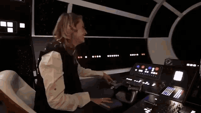 a woman is sitting at a steering wheel in a star wars simulator .