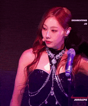 a woman is singing into a microphone while wearing a necklace .