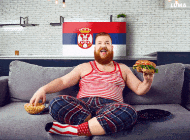 a man is sitting on a couch eating a sandwich in front of a luma sign