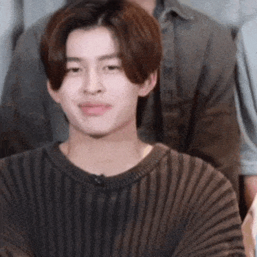 a young man wearing a brown striped sweater is sitting in front of a group of people .