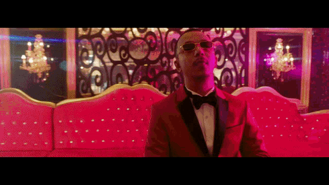 a man in a tuxedo and sunglasses is sitting on a pink couch