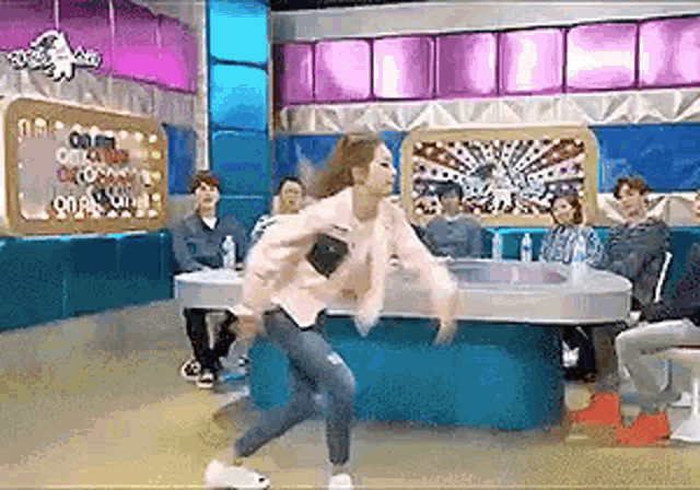 a woman in a pink jacket is dancing in front of a group of people sitting at a table .