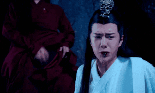 a man in a white robe is making a funny face while a woman in a red dress is standing behind him .