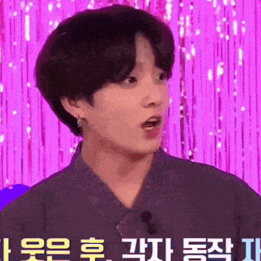a young man with a surprised look on his face is standing in front of a purple curtain .