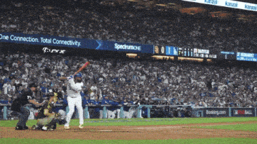 a baseball player swings at a pitch in front of a spectrumone advertisement