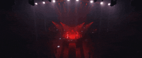 a group of people are standing on a stage with red lights