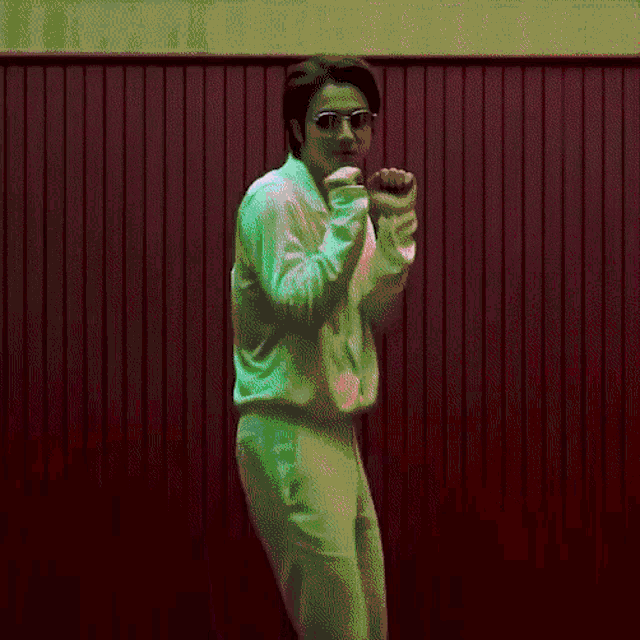 a man in a white shirt and green pants is standing in front of a red wall .