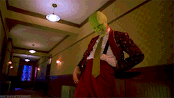 a man in a suit and tie with a green mask on his face is standing in a hallway