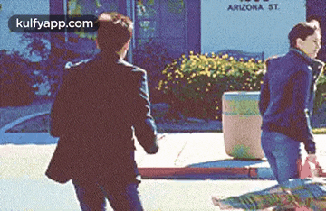 two men are walking down a sidewalk in front of a building that says arizona st. on it