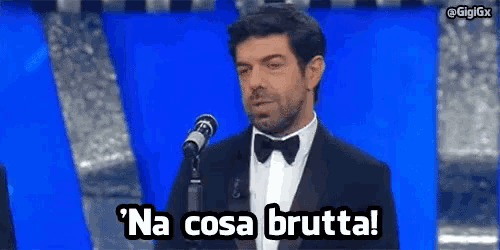 a man in a tuxedo is speaking into a microphone and says na cosa brutta !