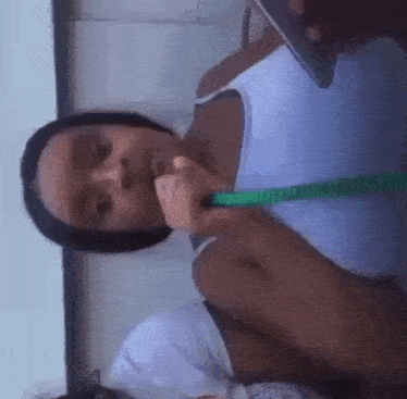a woman in a white tank top is smoking a hookah while looking at her phone .