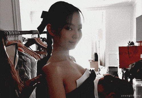 a woman is standing in a room with clothes hanging on a rack and the name youngtiffany is on the bottom of the image