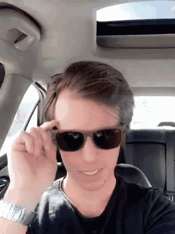 a man wearing sunglasses is sitting in a car with the sunroof open