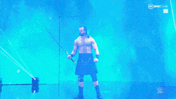 a wrestler in a kilt is holding a sword on a stage